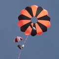 Orange and black rocketry and drone parachute with red and white drogue parachute fully expanded in air after ejection